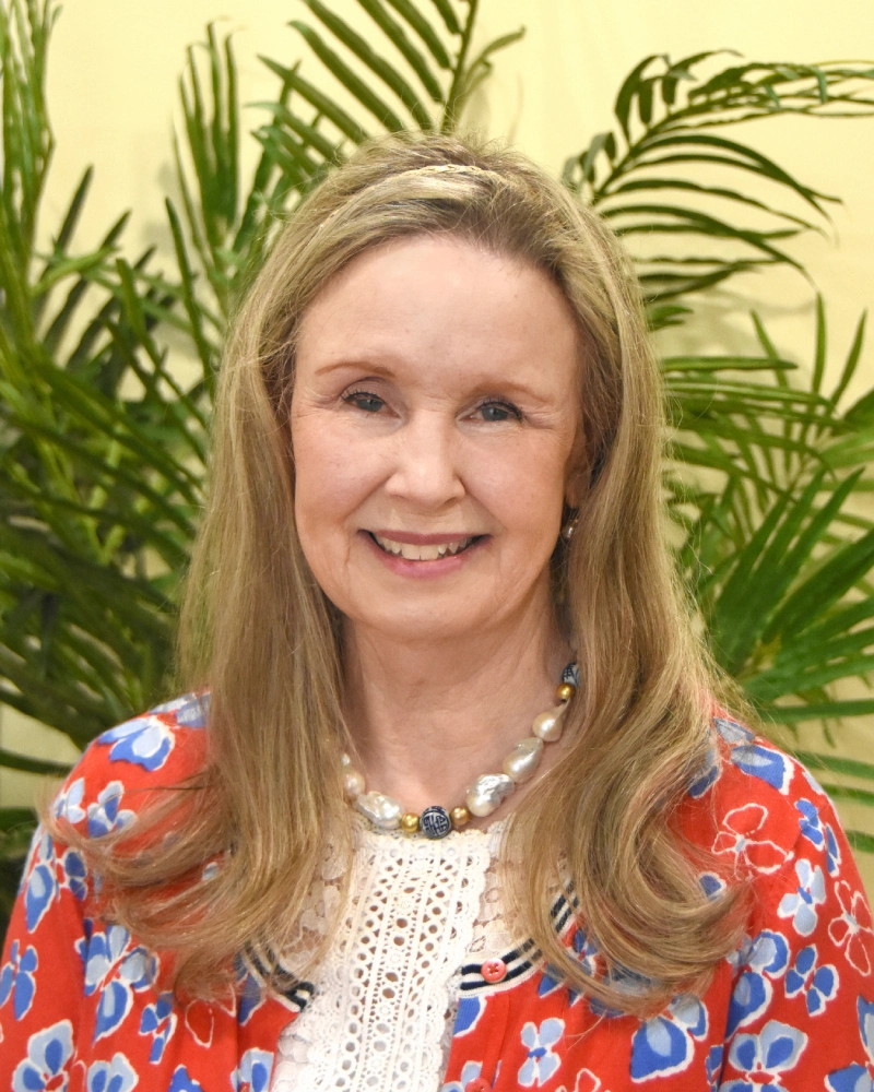 A woman with long blonde hair wearing a floral shirt.